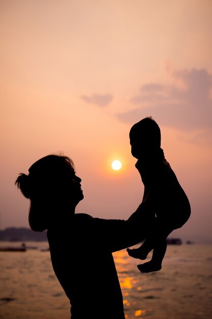 Silhouet van moeder het spelen met haar peuter bij zonsondergang