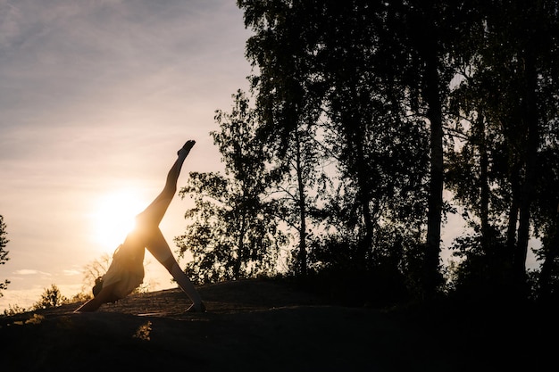 Silhouet van onherkenbare vrouw die ThreeLegged DownwardFacing Dog yoga asana pose in avond bij zonsondergang beoefenen Meisje Eka Pada Adho Mukha Svanasana houding buiten uitvoeren