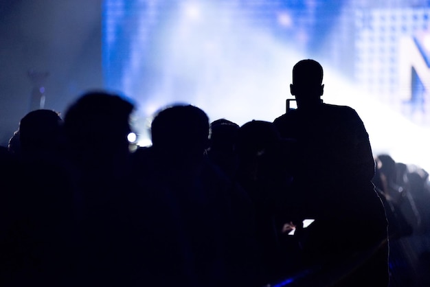 Silhouet van opgeheven handen die een smartphone vasthouden die muziek opneemt, concerten op het podium in de achtergrond