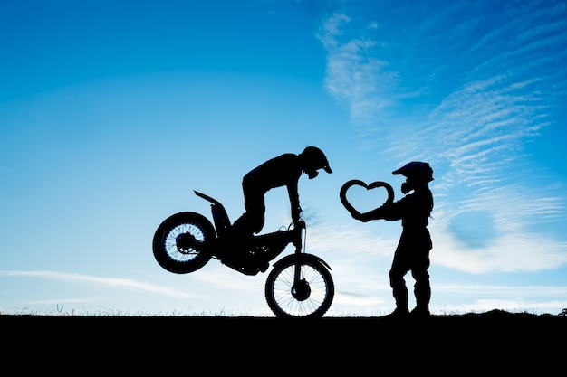 Silhouet van paar die zich met een motorfiets in de dag bevinden