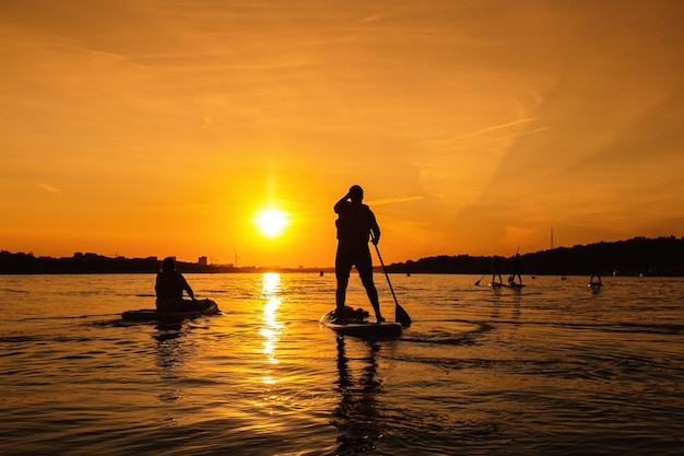 Silhouet van persoon die op sapboard op stadsrivier opstaat bij zonsondergang kleine lokale reis