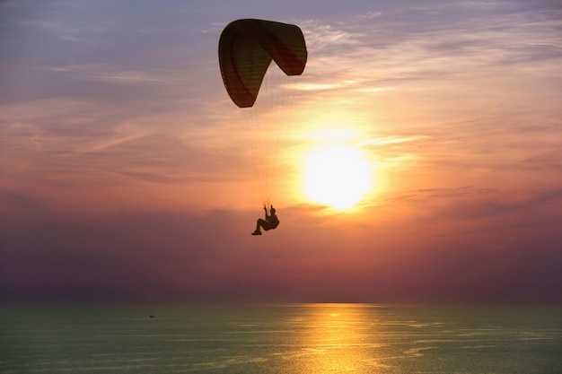 Silhouet van persoon in parachute bij zonsondergang boven zee in Phuket Thailand Man paragliding in de schemering