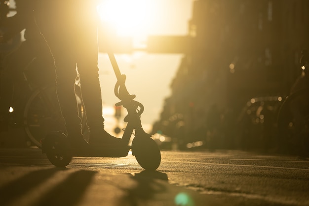 Silhouet van persoon op elektrische kick scooter in de stad tijdens zonsondergang concept van alternatieve trans...
