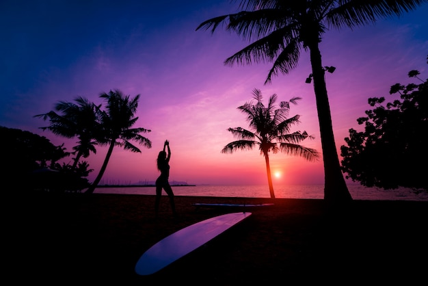 Silhouet van surfer meisje met lange surfplank bij zonsondergang op tropisch strand