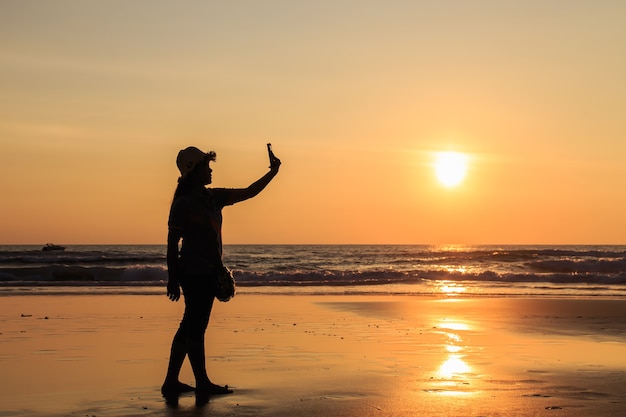 Silhouet van thaise vrouw die smartphone gebruiken bij het strand in zonsondergangtijd