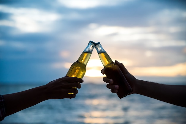 Silhouet van twee mensen die flessen bier samen kloppen tijdens zonsondergang.