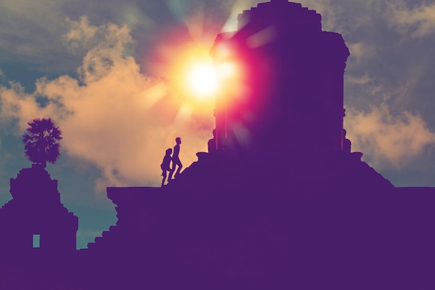 Foto silhouet van twee personen met zonlicht stap op trappen naar de top van een heilige oude tempel om een pelgrimstocht te maken