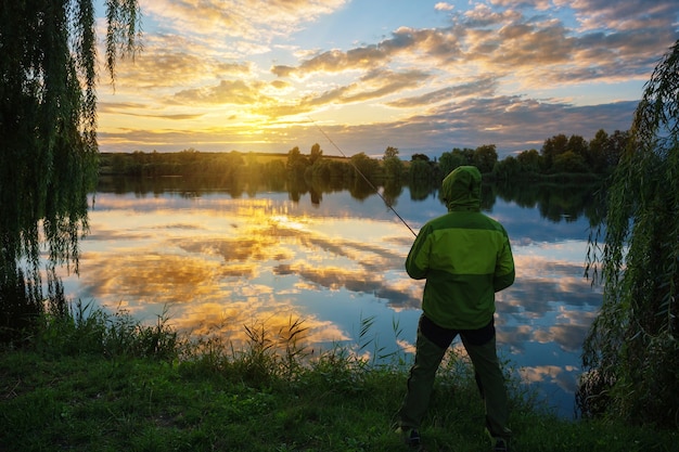 Silhouet van visser met hengel bij zonsondergang door lake