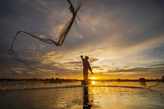 Silhouet van visser op vissersboot met netto op het meer bij zonsondergang, thailand