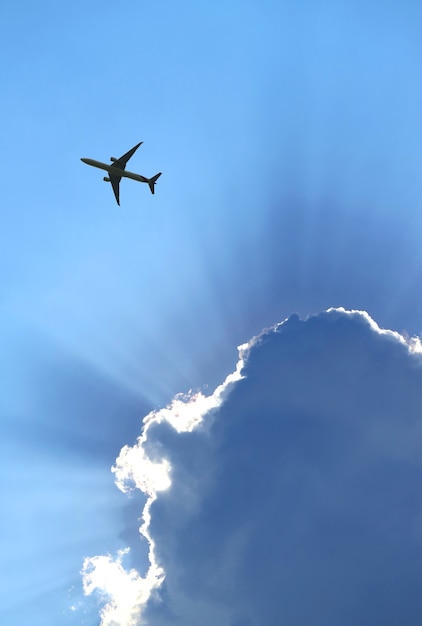 Silhouet van vliegtuig dat in de blauwe bewolkte hemel vliegt met verbazingwekkende zonnestralen