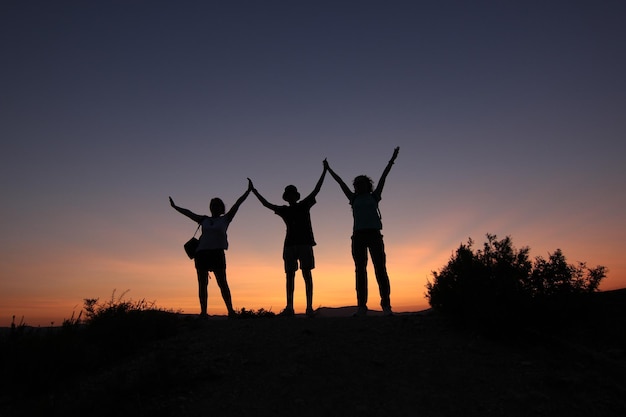 Silhouet van vrienden met armen omhoog, zonsondergangachtergrond