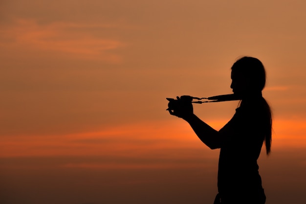 Silhouet van vrouw die met camera bij zonsondergang schieten