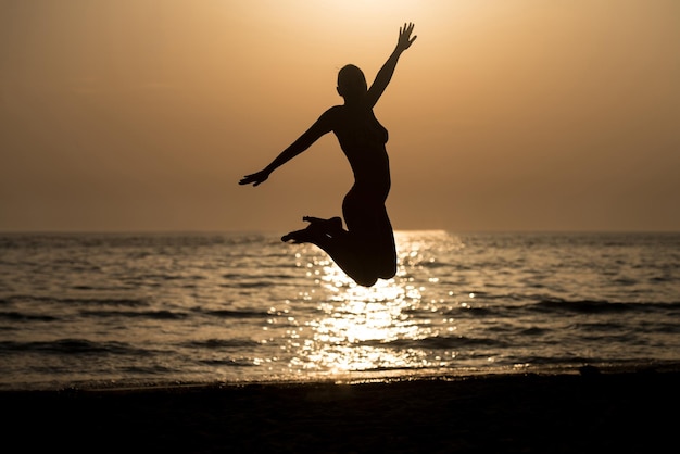 Silhouet van vrouw met opgeheven handen en rondspringen op het strand bij zonsondergang Copy Space Text