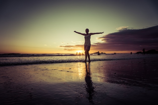 Silhouet van vrouw op sunset beach, meisje met open armen over zeekust. vrijheidsconcept