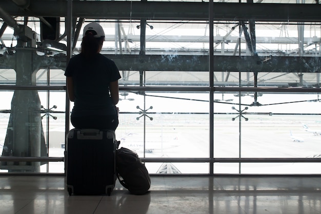 Silhouet van vrouw zitten op bagage koffer wachten op vlucht op de luchthaven