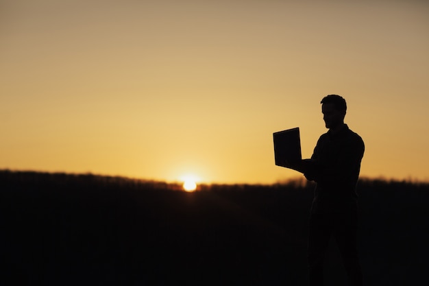 Silhouet van zakenman die met laptop werkt bij zonsondergang