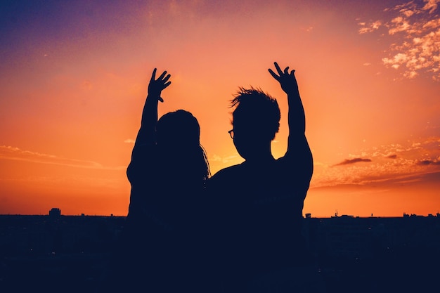 Silhouet vrienden met armen opgeheven tegen de hemel tijdens zonsondergang