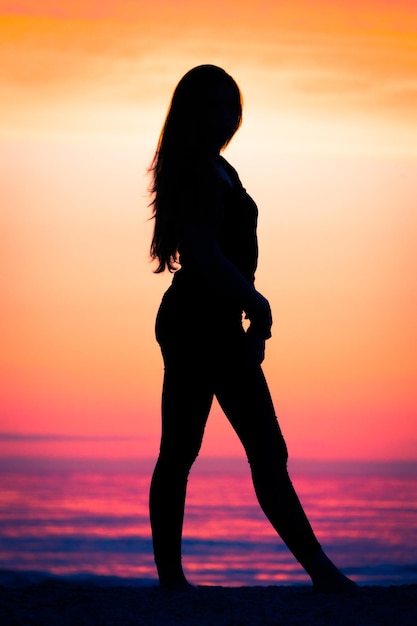 Silhouet vrouw die op het strand staat tegen de hemel tijdens de zonsondergang