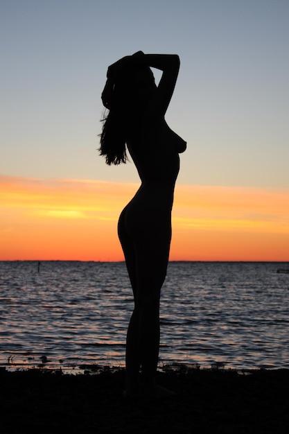 Foto silhouet vrouw die op het strand staat tegen de hemel tijdens de zonsondergang