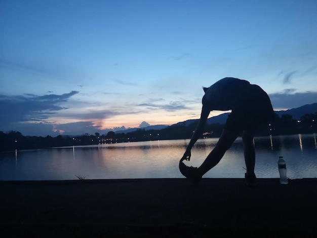 Foto silhouet vrouw die op het voetpad bij het meer staat tegen de hemel tijdens de zonsondergang