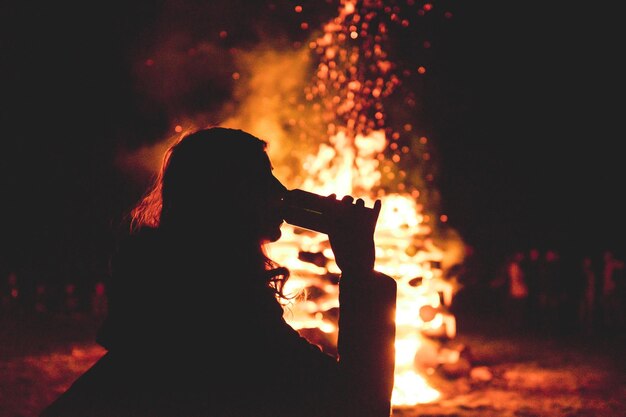 Foto silhouet vrouw drinkt terwijl ze tegen het vuur staat