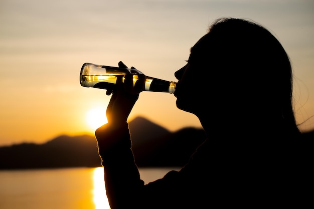 Silhouet vrouw drinkwater op het strand in de schemering