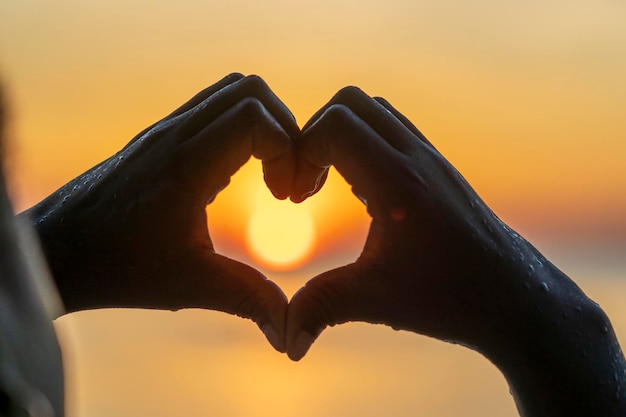 Silhouet vrouw handen in de vorm van een liefdeshart bij zonsondergang Vrouwelijke handen in de vorm van een hart tegen de lucht en de zee close-up