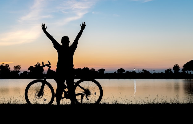 Silhouet vrouw handen omhoog met fiets op zonsondergang achtergrond