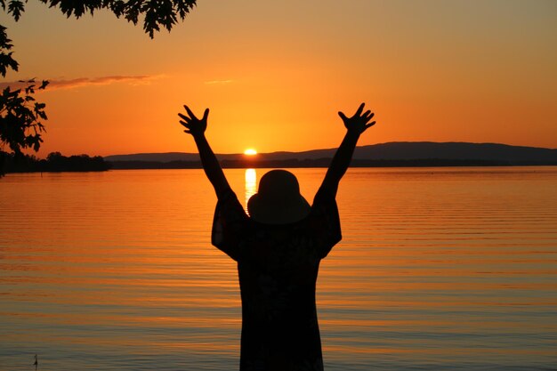 Foto silhouet vrouw met uitgestrekte armen staande tegen de oranje hemel