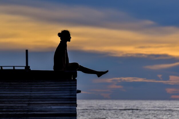 Silhouet vrouw zit over de zee tegen de hemel tijdens de zonsondergang