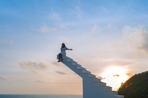 Silhouet winderig haar Aziatische vrouw zit bovenop een houten trap met avondrood op de achtergrond, vrijheid, succesconcept