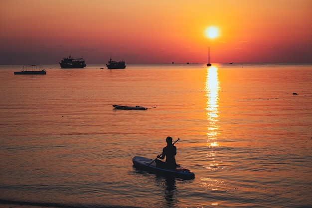 Silhouetbeeld van een jonge vrouw die voor zonsondergang op een stand-up paddleboard in de zee zit