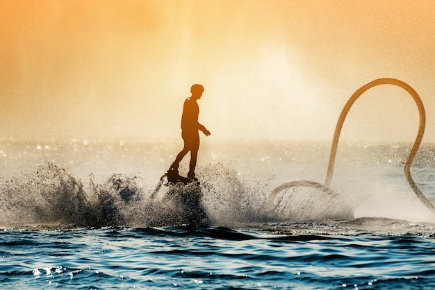 Foto silhouetbeeld van een man die het vliegbord (aqua-bord) op zee tonen, de nieuwe spectaculaire sport
