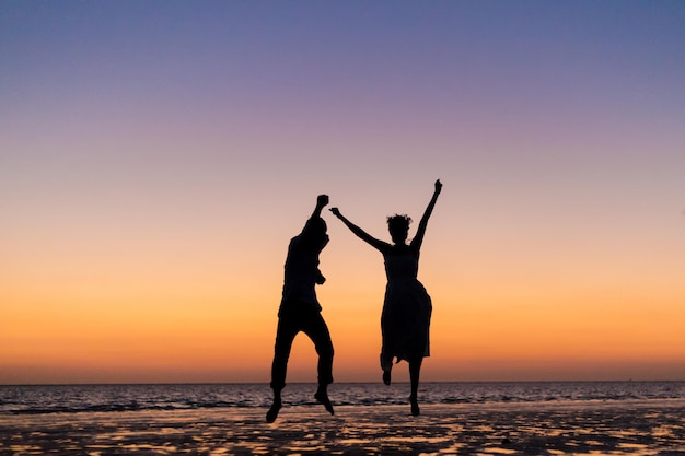 Silhouetmensen die tijdens zonsondergang op het strand tegen de hemel staan