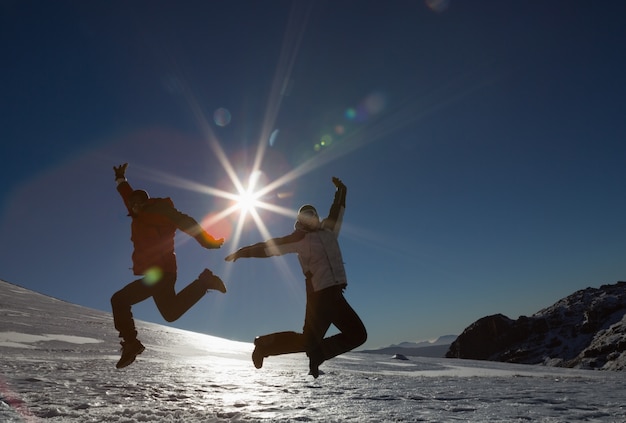 Silhouetpaar die op sneeuw tegen zon en blauwe hemel springen