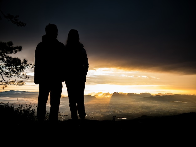 Silhouetpaar die zich op bergen met zonsopgang bevinden