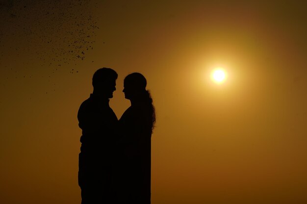 Silhouetpaar staat tegen de oranje hemel tijdens de zonsondergang