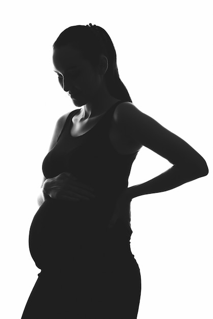 Foto silhouetportret van zwangere vrouw op witte achtergrond met handen op buik, verticaal beeld, ivf-zwangerschapsconcept