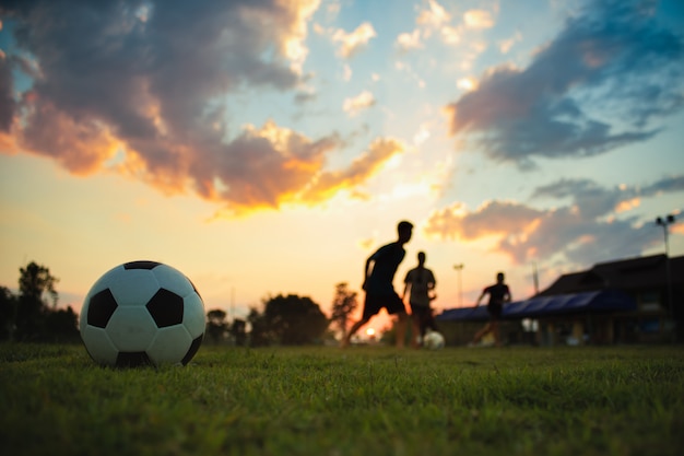 Silhouette action sport outdoors of a group of kids having fun playing soccer football 