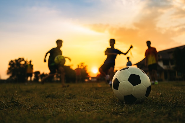 석양 아래 운동을 위해 축구 축구를하는 재미 아이의 야외 실루엣 액션 스포츠.