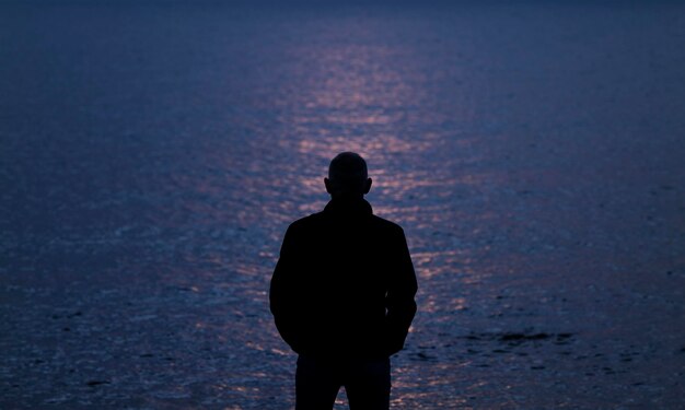 Foto silhouette di un uomo adulto che guarda il mare durante il tramonto