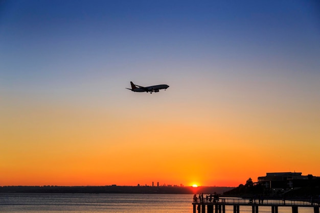 日没時に海に近い滑走路に近づく飛行機のシルエット