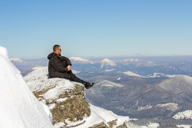 Silhouette of alone tourist sitting on snowy mountain top enjoying view and achievement on bright sunny winter day. Adventure, outdoors activities, healthy lifestyle.