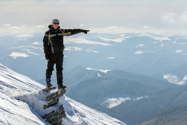 Silhouette of alone tourist standing on snowy mountain top in winner pose with raised hands enjoying view and achievement on bright sunny winter day. Adventure, outdoors activities, healthy lifestyle.