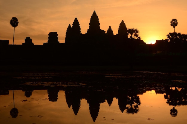 Силуэт Ангкор-Ват у озера на фоне неба во время захода солнца