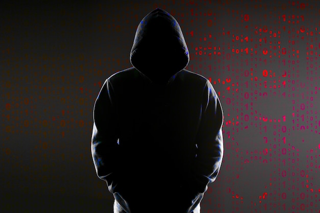 Silhouette of an anonymous hacker in the hood on the binary code