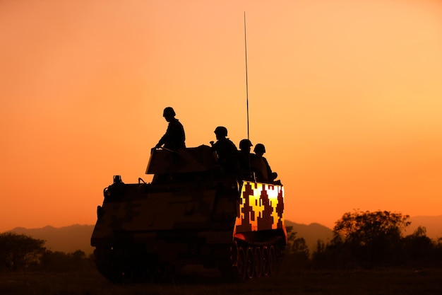 Silhouette army soldier sitting on vehicle against orange sky