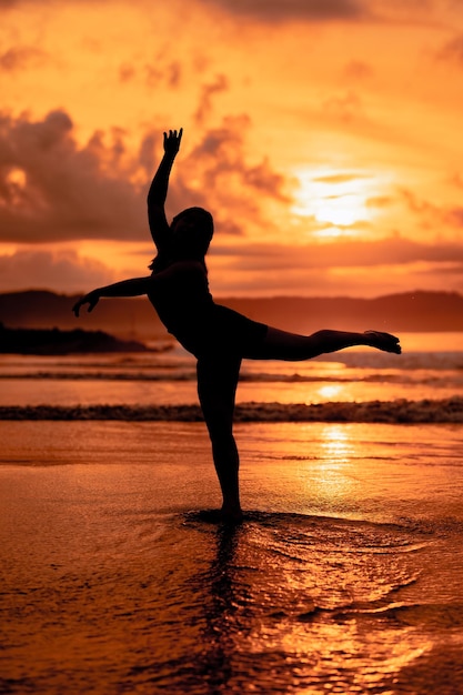 Silhouette of an Asian woman dancing ballet with great flexibility and a view of the waves behind her