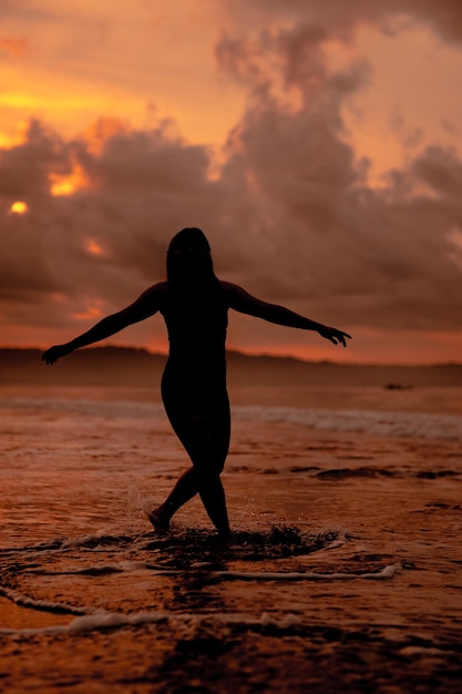 Силуэт азиатской женщины, играющей в воде на пляже с сильными волнами