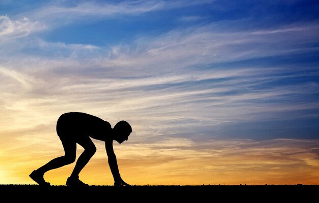 Silhouette of athlete in position to run on sunset background